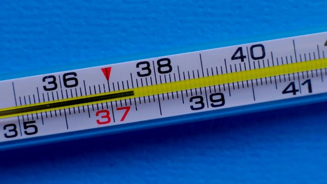 Glass mercurial thermometer shows high temperature of the body on blue background. Temperature increase. 4k. Close-up. Tracking shot. 