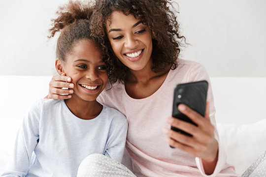 Image of american woman and her little daughter using cellphone at home