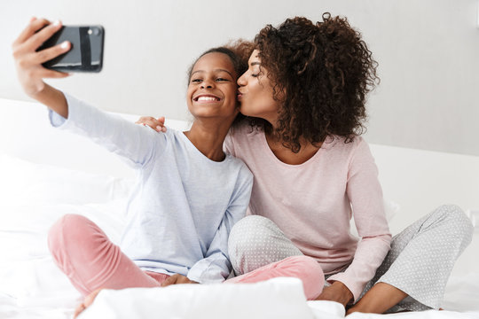 Image of american woman and little daughter taking selfie at home