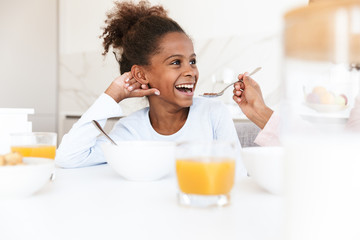 Fototapeta premium Image of american woman feeding her daughter while having breakfast