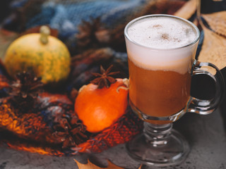 a glass of pumpkin spiced latte on the table with a colorful scarf and cinnamon and autumn leaves