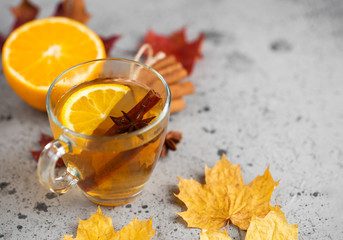 a Cup of hot tea with orange and cinnamon on a stone table with dry autumn leaves