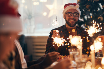 Portrait of cheerful bearded man wearing santa hat while enjoying Christmas celebration dining with...