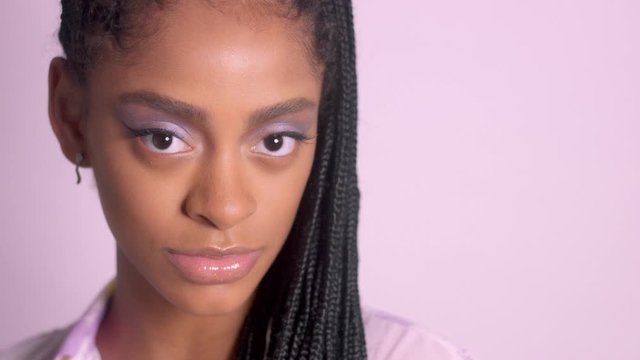 Mixed race woman with pink lilac makeup glowy skin and hair braids poses to a camera, closeup portrait Ideal strobbing skin