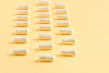 Row of medical capsules for health care with selective focus on neutral yellow background. Pharmacology supplements on yellow backdrop with empty space for text. Medicine pills. Vitamins