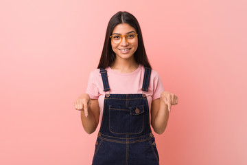Young pretty arab woman wearing a jeans dungaree points down with fingers, positive feeling.
