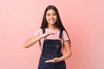 Young pretty arab woman wearing a jeans dungaree holding something with both hands, product presentation.
