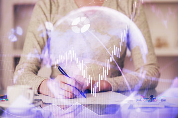 Hand taking notes in notepad. Forex chart holograms in front. Concept of research. Double exposure