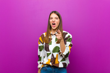 young pretty woman pointing at camera with an angry aggressive expression looking like a furious,...