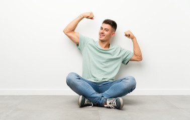 Young handsome man sitting on the floor celebrating a victory