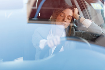 Young businesswoman with eyes closed behind the steering wheel.