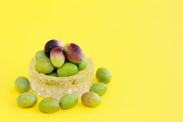 natural fresh round green and brown olives in a decorative glass plate on a yellow background