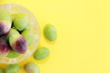 natural fresh round green and brown olives in a decorative glass plate on a yellow background