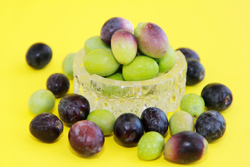 natural fresh round green and brown olives in a decorative glass plate on a yellow background