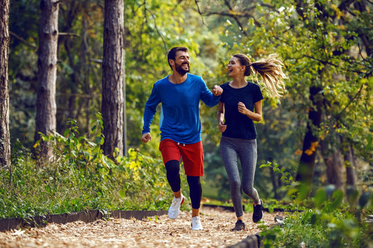 Full length of fit sporty happy caucasian couple in sportswear running in woods on trail in morning.