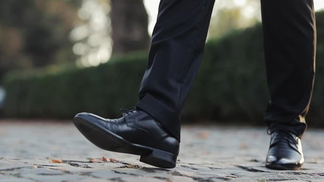 Man in black shoes stepping forward Person moving forward outdoor. Walking on the floor, close-up view of man's leather shoes