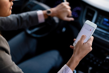 Close-up of woman using smart phone behind the wheel.
