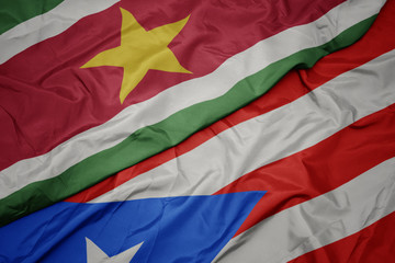 waving colorful flag of puerto rico and national flag of suriname.