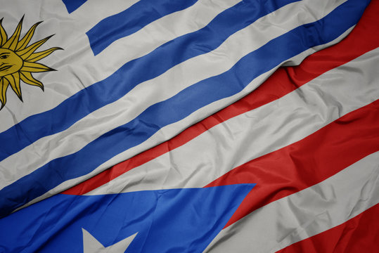 waving colorful flag of puerto rico and national flag of uruguay.