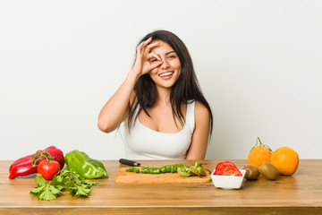 Young curvy woman preparing a healthy meal excited keeping ok gesture on eye.