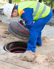 worker in a blue uniform and yellow vest, opens the collector cover for electrical communications