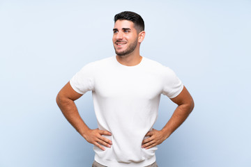 Caucasian handsome man over isolated blue background posing with arms at hip and smiling