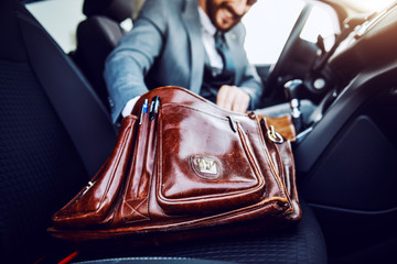 Businessman sitting in his car and taking out something from his briefcase. Selective focus on...