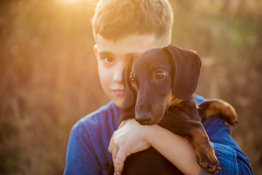 Young Boy Hugging Black Dog Outdoors. Friendship, Love And Relationship Concept