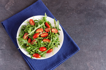 Fototapeta na wymiar Salad with fresh green arugula and tomato cherry in a white ceramic bowl.