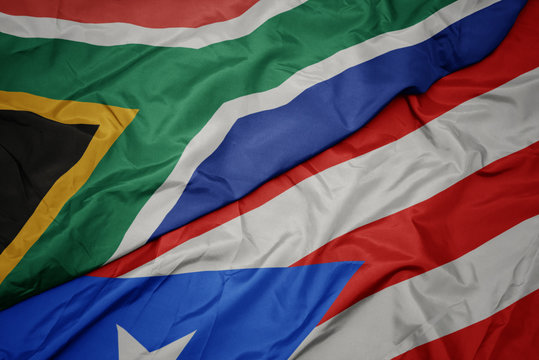waving colorful flag of puerto rico and national flag of south africa.