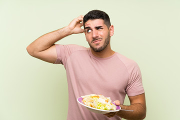 Young handsome man with salad over isolated green wall having doubts and with confuse face expression