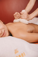 Fototapeta premium cropped view of masseur doing back massage with herbal balls to woman in spa