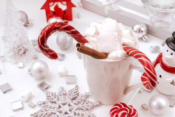 Obraz na płótnie Canvas hot chocolate, cocoa with marshmallows and lollipops, silver balls, candle, snowflake, transparent Christmas tree, Christmas decor, cinnamon, snowman, snow, top view