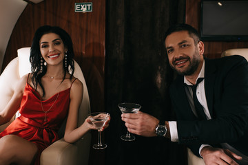 happy man and woman in red dress holding martini glasses in private jet
