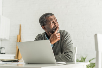thoughtful african american man looking away while sitting near laptop