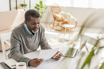 selective focus of senior african american man looking at utility bill while sitting near laptop - Powered by Adobe