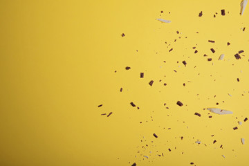 White and dark chocolate pieces and chipson on a bright yellow background. View from above. Flat lay.