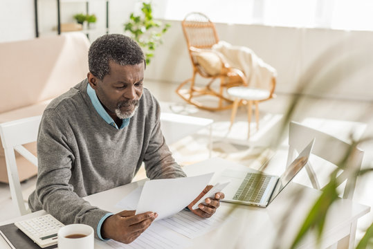 selective focus of senior african american man looking at utility bill while sitting near laptop