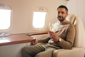 cheerful man holding champagne glass while sitting in first class of private jet