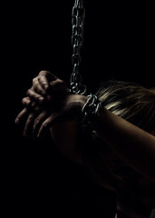 White women's hand are on the floor chained metal chains close-up on a black background, toned to a...