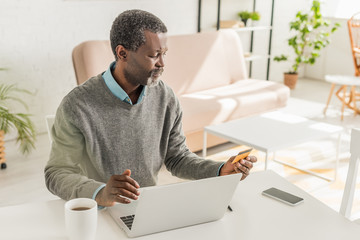 senior african american man sitting near laptop and holding credit card