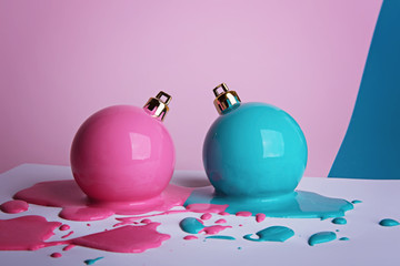 Two New Year's Christmas balls painted in pale pink and turquoise lay in a puddles of paint on a white sheet of paper.