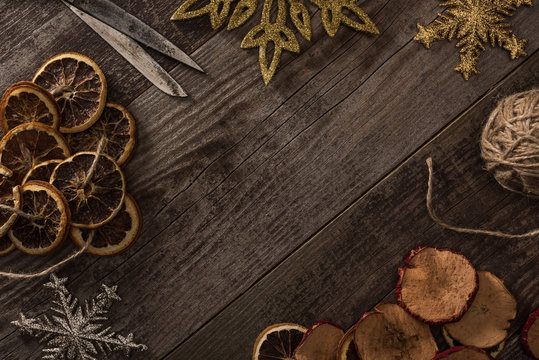 top view of dried citrus and apple slices near snowflakes, rope and scissors on wooden surface with copy space