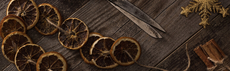 top view of dried citrus slices on rope near snowflake, cinnamon and scissors on wooden surface,...