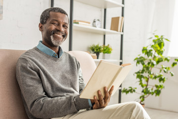 cheerful african american man holding book and smiling at camera