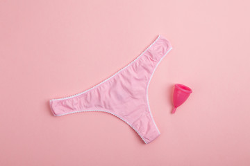 Pink women's panties with menstrual cup on pink background. Concept of menstruation and women's health.