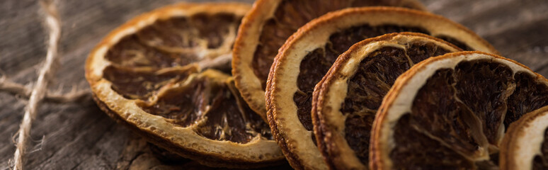 close up view of dried orange slices on rope on wooden surface, panoramic shot