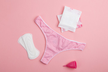 Different types of feminine hygiene products-menstrual cups, sanitary pads and tampons. Pink women's panties with sanitary napkins, tampons, menstrual cup on pink background. Concept of menstruation. 