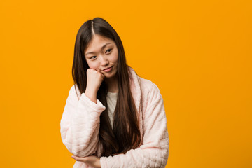 Young chinese woman in pajama who feels sad and pensive, looking at copy space.