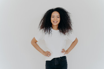 Half length shot of beautiful cheerful millennial girl stands with happy face expression against...